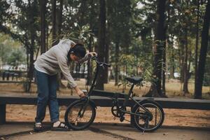 contento asiatico giovane donna camminare e cavalcata bicicletta nel parco, strada città sua sorridente utilizzando bicicletta di trasporto, eco amichevole, persone stile di vita concetto. foto