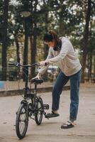 contento asiatico giovane donna camminare e cavalcata bicicletta nel parco, strada città sua sorridente utilizzando bicicletta di trasporto, eco amichevole, persone stile di vita concetto. foto