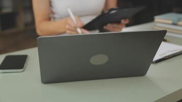 asiatico donna d'affari Lavorando su il computer portatile computer Guarda per lavoro in linea, libero professionista guardare e digitando su taccuino su tavolo, stile di vita di donna studiando in linea foto