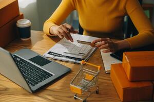 giovane donna Tenere un' smartphone, tavoletta mostrando pagamento successo e credito carta con giallo pacco scatola come in linea shopping concetto nel ufficio foto