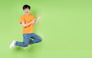 giovane uomo asiatico che salta, isolato su sfondo verde foto