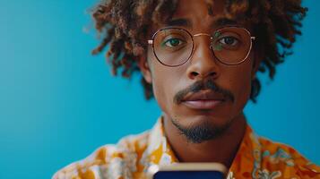 ai generato un attraente giovane afro uomo è utilizzando il suo mobile Telefono mentre in piedi vicino un' enorme smartphone al di sopra di un' blu studio sfondo. Questo è un' modello per un' sito web o applicazione con spazio per foto