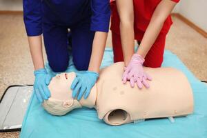 cpr. squadra medici lavori su manichino indossatrice indiretta cardiaco massaggio e artificiale ventilazione polmoni. Due giovane ragazze infermiera impegnato simulatore ospedale camera. paramedici emergenza situazione foto