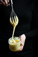 fresco fatti in casa zuccherato condensato latte nel un' vaso e un' cucina frusta. su un' nero sfondo. foto