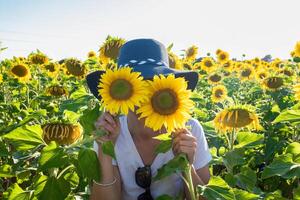 donna con cappello giocando con Due impianti di girasoli foto