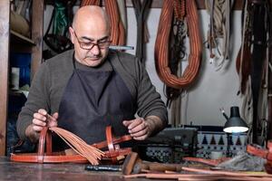 artigiano Lavorando il pelle nel il suo piccolo selleria laboratorio foto