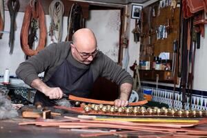 artigiano Lavorando il pelle nel il suo piccolo selleria laboratorio foto