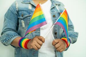 la signora asiatica che indossa braccialetti con bandiera arcobaleno e tiene il cuore rosso, simbolo del mese dell'orgoglio lgbt celebra l'annuale a giugno sociale di gay, lesbiche, bisessuali, transgender, diritti umani. foto