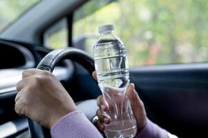 autista donna asiatica che tiene una bottiglia per bere acqua durante la guida di un'auto. la borsa dell'acqua calda in plastica provoca un incendio. foto