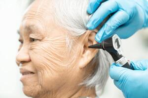 audiologo o ent medico uso otoscopio controllo orecchio di asiatico anziano donna paziente trattamento udito perdita problema. foto