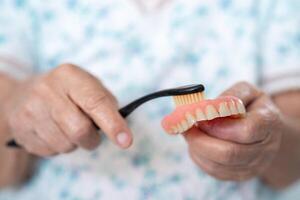 asiatico anziano donna paziente uso spazzolino per pulito parziale dentiera di sostituzione denti. foto