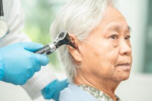 audiologo o ent medico uso otoscopio controllo orecchio di asiatico anziano donna paziente trattamento udito perdita problema. foto