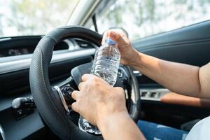 autista donna asiatica che tiene una bottiglia per bere acqua durante la guida di un'auto. la borsa dell'acqua calda in plastica provoca un incendio. foto