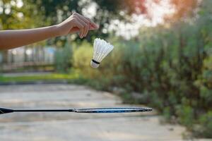 asiatico ragazza detiene un' bianca volano e lascia esso autunno gratuito su il badminton racchetta sotto. morbido e selettivo messa a fuoco. foto