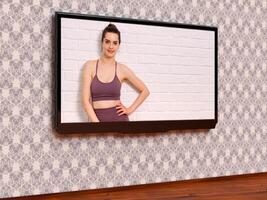 moderno tv con un' donna nel abbigliamento sportivo in posa contro bianca parete fatto di mattoni su suo schermo foto