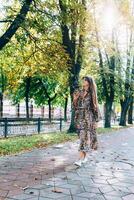 giovane donna nel occhiali da sole a piedi nel autunno parco con poco cucciolo. all'aperto stile di vita ritratto di bella sorridente femmina e sua piccolo cane. foto