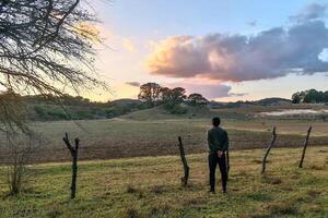 giovane uomo riflessivo e riflettendo, guardare a il tramonto con bellissimo nuvole e spazio per testo foto