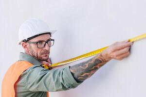 costruzione lavoratore ingegnere maschio professionale Guarda Lavorando misurare parete utilizzando metri nastro alto dettaglio precisione foto