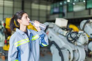 Salute cura donna lavoratore potabile pulito acqua mentre Lavorando nel fabbrica macchina magazzino per ricaricare e personale salutare foto