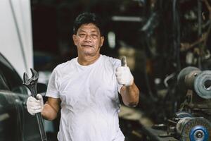 ritratto contento asiatico adulto maschio lavoratore sporco con olio Grasso in piedi pollici su sorridente foto