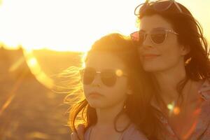 ai generato madre e figlia godendo tramonto a spiaggia con ai generato. foto