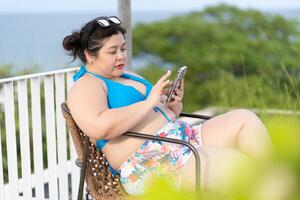 ritratto di asiatico più dimensione bellissimo donna indossare bikini e utilizzando smartphone durante vacanza foto