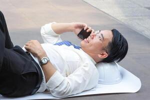 ingegnere uomo rilassante e utilizzando smartphone su il pavimento dopo Lavorando difficile foto