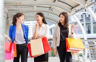 gruppo di giovane asiatico donne trasporto shopping borse mentre a piedi lungo il strada. contento vita e shopping concetti foto