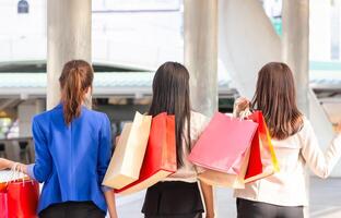 indietro Visualizza di un' gruppo di giovane donne trasporto shopping borse mentre a piedi lungo il strada. contento vita e shopping concetti foto