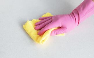 un' mano nel un' rosa guanto salviette il superficie con giallo microfibra. alto qualità foto