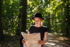 giovane caucasico donna nel cappello guardare a geografico carta geografica nel il ombra di alberi nel un' parco o foresta. alto qualità foto