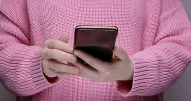 mani un' ragazza nel un' rosa maglione Tenere un' nero smartphone. alto qualità foto