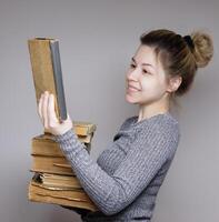 giovane femmina alunno guardare e sorridente guardare a un' libro. detiene molti vecchio libri nel sua mani. selettivo messa a fuoco. foto