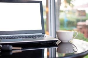 bianca Schermo il computer portatile con caffè tazza su bicchiere tavolo foto