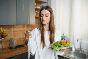 contento giovane donna preparazione insalata nel cucina. salutare dieta foto