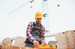 installazione mattone parete. costruzione lavoratore nel uniforme e sicurezza attrezzatura avere lavoro su edificio foto