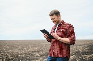 un' contadino nel stivali lavori con il suo tavoletta nel un' campo seminato nel primavera. un agronomo passeggiate il terra, valutare un' arato campo nel autunno. agricoltura. inteligente agricoltura tecnologie foto