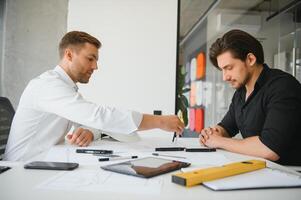 Due giovane architetti con progetti di un' Casa in piedi nel ufficio, parlando. foto