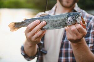 contento pescatore Tenere un' pesce catturato. pesca su il bellissimo fiume. foto