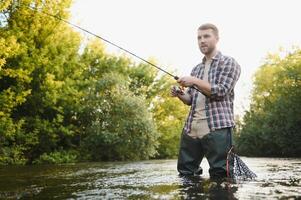 uomo con pesca asta, pescatore uomini nel fiume acqua all'aperto. attraente trota pesce nel rete. estate pesca passatempo foto