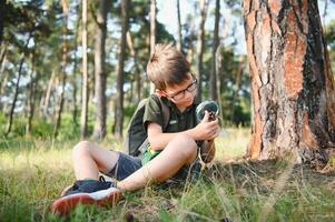 scolaro è esplorando natura con ingrandimento bicchiere. estate vacanza per curioso bambini nel foresta. escursionismo. boy-scout. foto