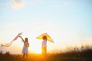 bambini lanciare un' aquilone nel il campo a tramonto foto