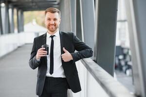 vicino su grave uomo d'affari potabile prendere lontano caffè a strada. ritratto di attività commerciale uomo in attesa con caffè per partire all'aperto. ufficio dipendente guardare lontano a strada. maschio professionale prendere rompere foto