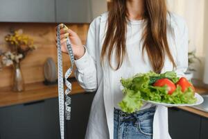 contento giovane donna preparazione insalata nel cucina. salutare dieta foto