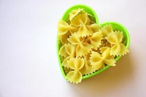 farfalla sagomato pasta impilati nel un' cuore forma su il tavolo. foto