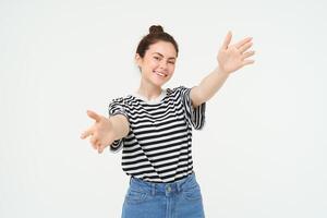 ritratto di carino sorridente donna tratti sua mani, raggiunge per hold qualche cosa, vuole per abbraccio voi, in piedi al di sopra di bianca sfondo foto