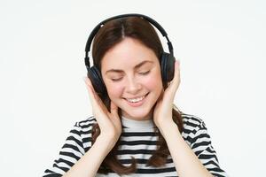 ritratto di donna, sorridente, indossare senza fili cuffia, ascoltando musica, studiando nel auricolari, in piedi isolato al di sopra di bianca sfondo foto