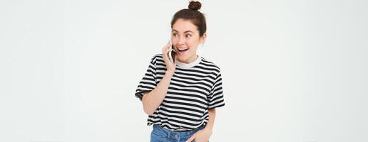 ritratto di entusiasta giovane donna parlando su mobile Telefono, chat con amico, reagisce per sorprendente notizia ricevuto di telefono, bianca sfondo foto