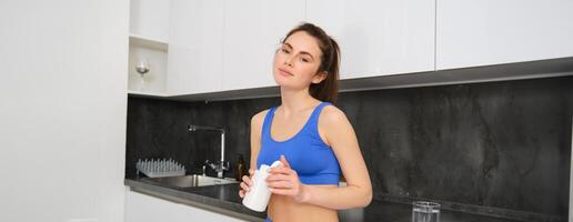 Immagine di giovane brunetta donna con magra, in forma corpo, Tenere dietetico integratori, vitamina b, pesce olio, in piedi nel cucina foto