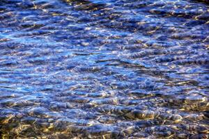 sfondo di il acqua di lago Traunsee nel il costiero la zona. colorato struttura di pietre sotto acqua foto